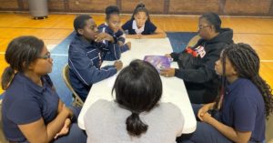 Group sits at table in gymnasium during Family Math Night