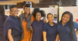 Group poses for photo in front of 2019 Science Fair project